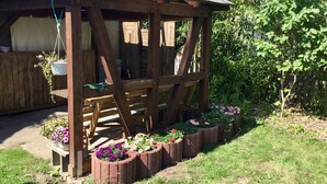 A wooden gazebo with a sloped roof, surrounded by flower beds with various flowers. - Ferienwohnung in Klutz an der Ostsee (Klütz)