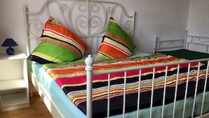 A bed with a white metal frame, colorful striped bedding, and two pillows with stripes. - Ferienwohnung in Klutz an der Ostsee (Klütz)