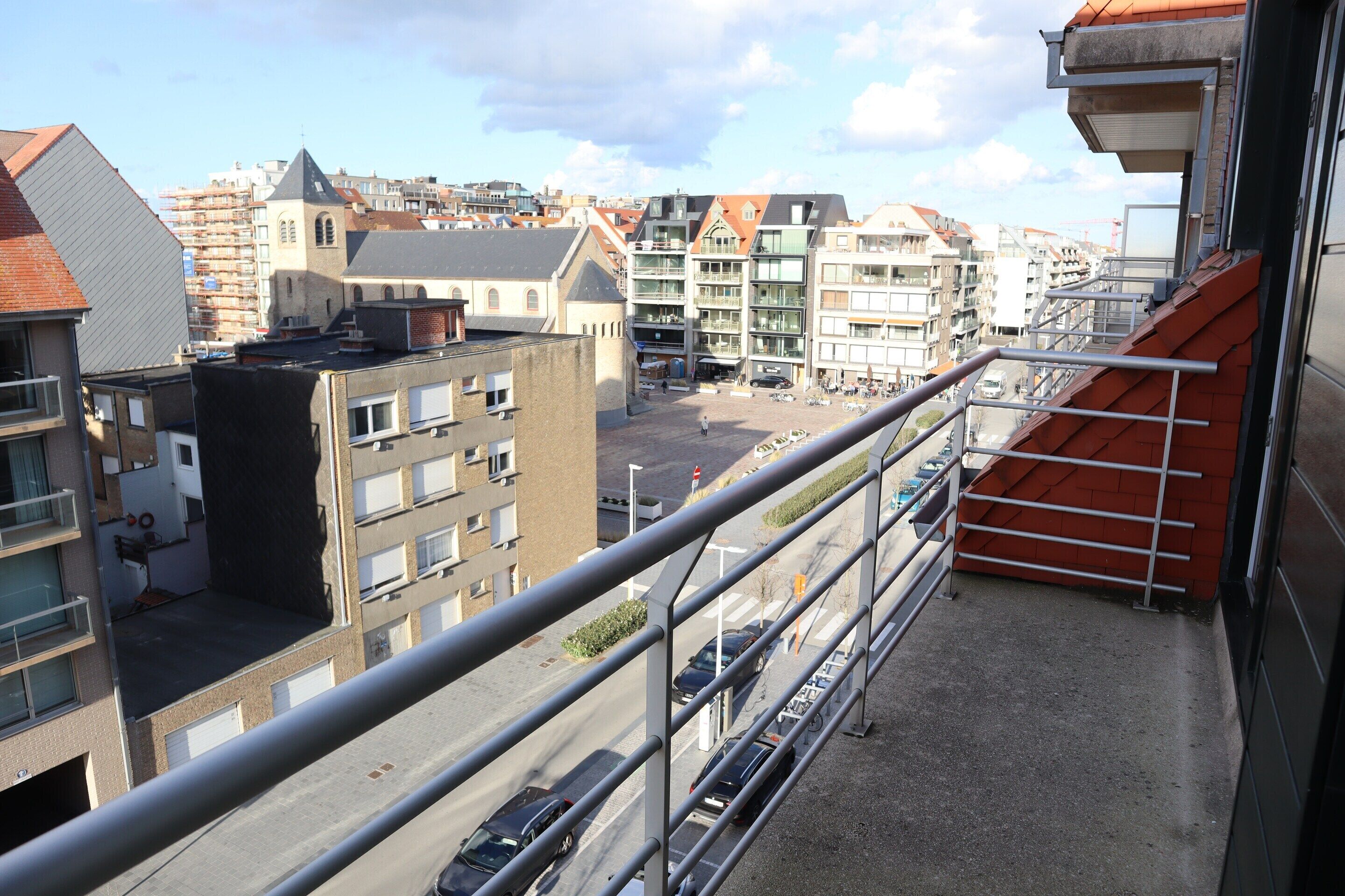A balcony with a metal railing overlooking a street with cars and buildings.