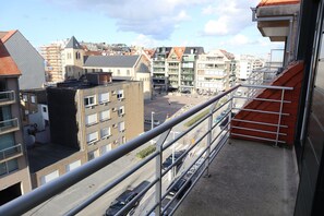Un balcon doté d’une rambarde en métal, donnant sur une rue animée par la circulation des voitures et bordée d’immeubles.