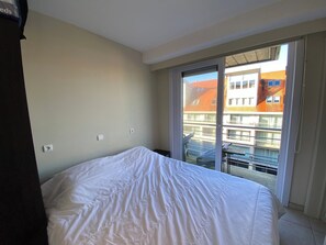 Une chambre d’hôtel avec un grand lit, une porte-fenêtre coulissante donnant sur un balcon et une vue sur les bâtiments environnants.