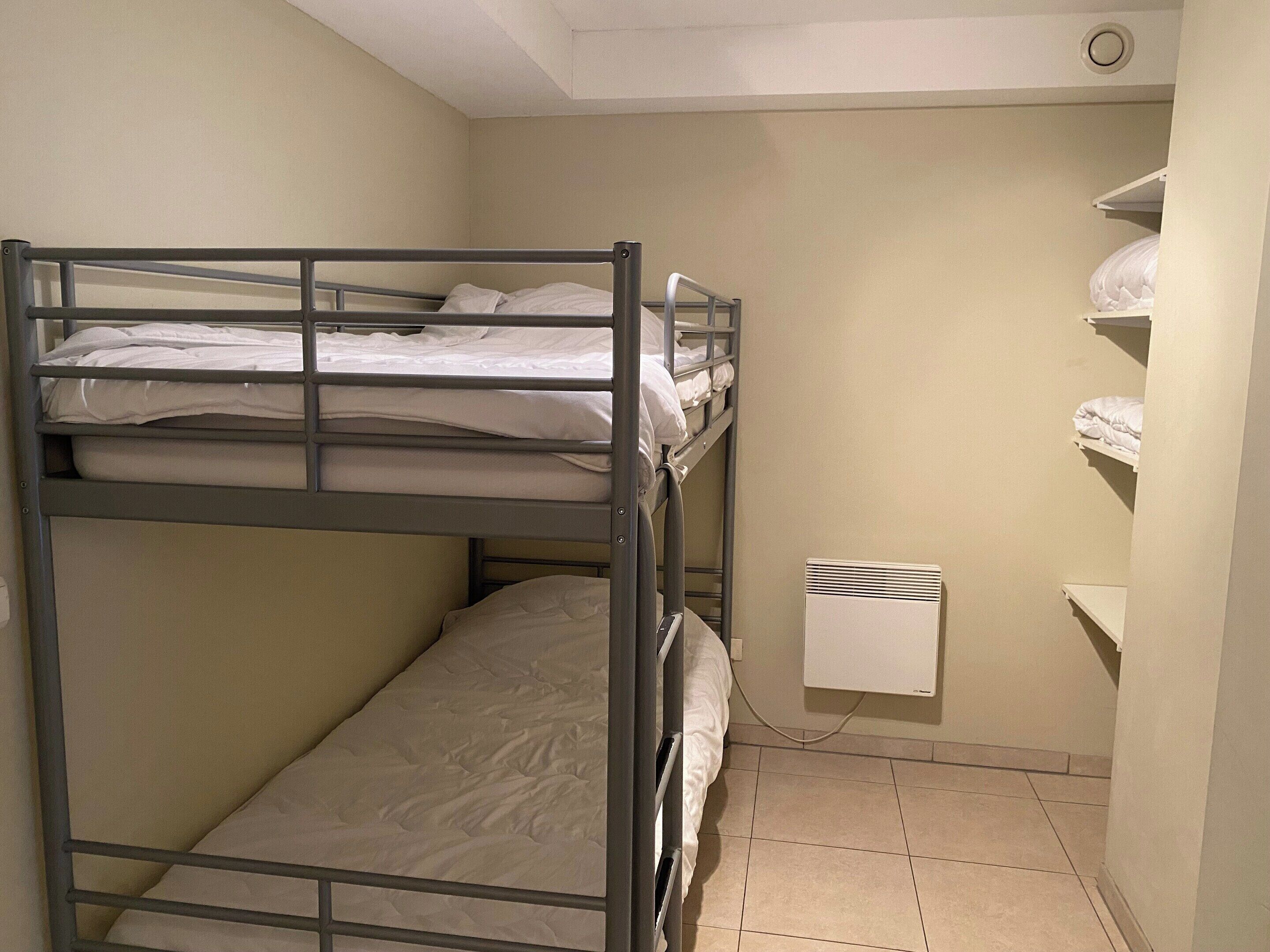 A bunk bed room with a white heater and a shelf with folded blankets.