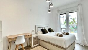A modern bedroom with a bed, a desk, and a chair. There is a window with curtains and a view of buildings outside. - Belvilla by OYO Playa Granada Beach & Golf 9 (Motril)