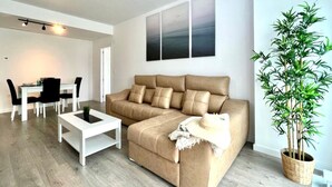 A modern living room with a beige sofa, a white coffee table, and a dining area with a white table and black chairs. - Belvilla by OYO Playa Granada Beach & Golf 9 (Motril)