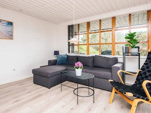 A modern living room with a sectional sofa, a small round table, a chair, and a large window with a view of greenery.