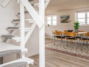 Un intérieur moderne avec un escalier blanc, un coin repas comprenant une table et des chaises, et une grande fenêtre offrant une vue dégagée.
