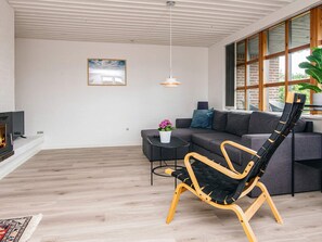 A modern living room with a fireplace, a sofa, a black chair, and a large window. - 7 Person Holiday Home in Ulfborg (Ulfborg)