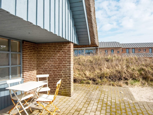 A building with a brick facade, a flat roof, and a paved patio area with a table and chairs.