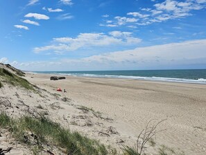 A beach with a dune, a red tent, and a black object on the sand. - 7 Person Holiday Home in Ulfborg (Ulfborg)
