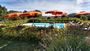 A pool area with orange umbrellas, lounge chairs, and a lamp post. - Villa Colombini Comfortable Holiday Residence (Trequanda)