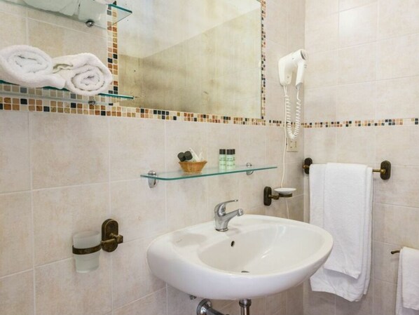 Et badeværelse med en hvid vask, en glashylde med toiletartikler, et håndklædestativ og en hårtørrer.