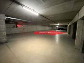 Un parking avec une flèche rouge indiquant une porte portant l’inscription « PASSAGE VERS L’ASCENSEUR ».
