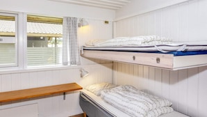 A dormitory room with bunk beds, a window with curtains, and a bedside table.