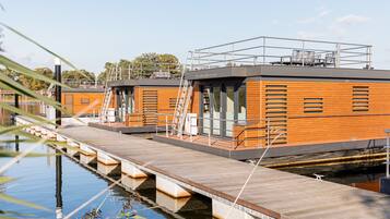 Un hotel flotante con fachada de madera, un espacio exterior cubierto y un muelle que se adentra en el agua.