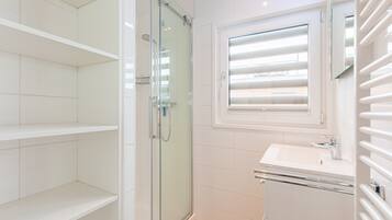 Une salle de bain moderne avec une douche à parois de verre, un lavabo blanc et une fenêtre équipée de stores.
