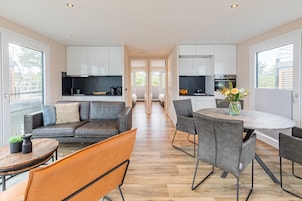 A modern kitchen with white cabinets, a dining area with a round table and chairs, and a sofa with cushions.