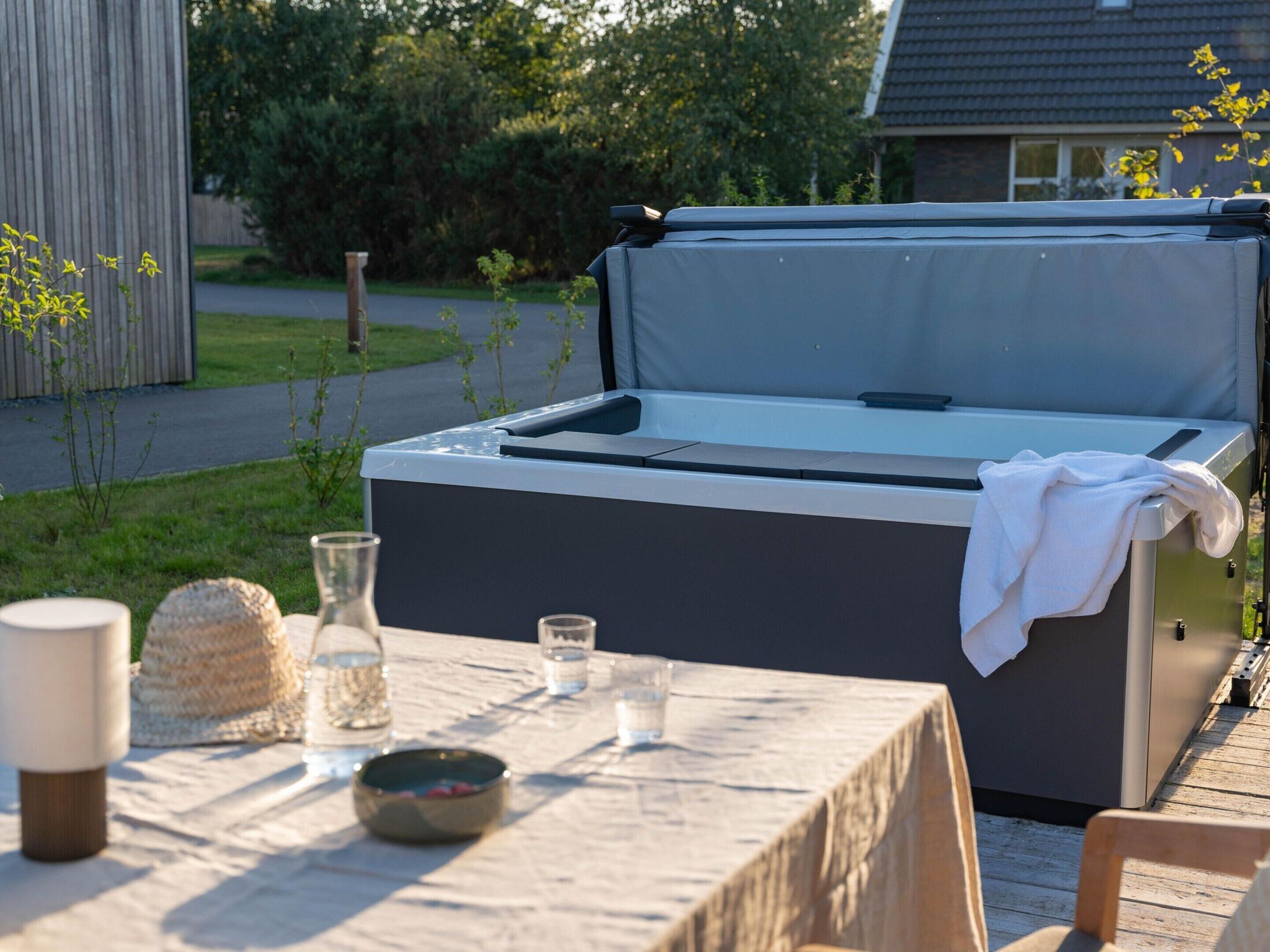 A hot tub with a table set up nearby, including a glass, a bowl, and a candle.