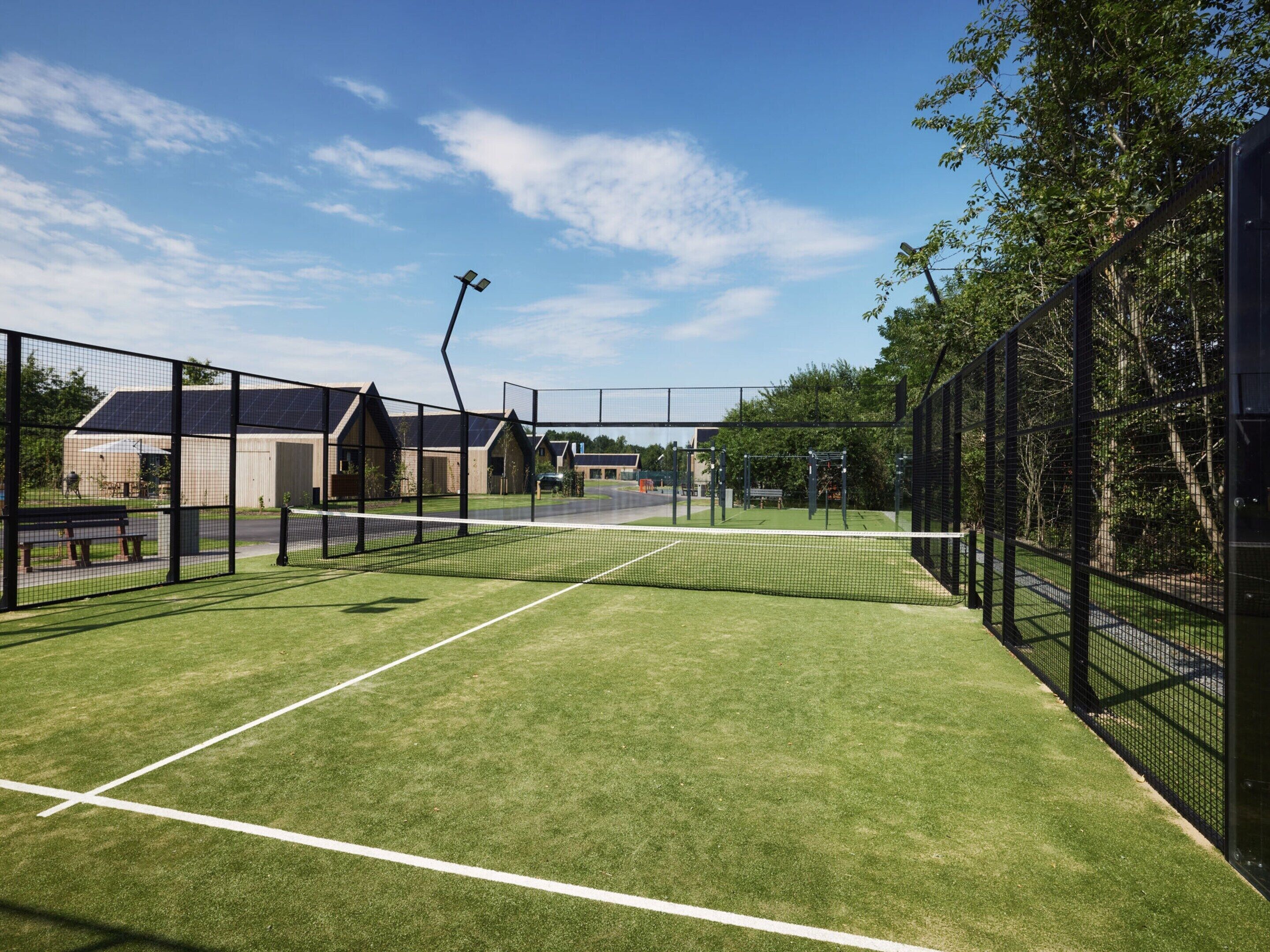 A tennis court with a net, surrounded by a fence, and buildings in the background.
