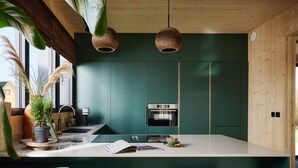 A modern kitchen with a central island, two bar stools, a built-in oven, and hanging pendant lights. - Luxury Villa in Drenthe With Outdoor Spa (Appelscha)