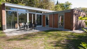 Una casa moderna con grandes puertas de vidrio, un patio con mobiliario exterior y fachada de ladrillo.