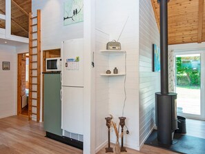 A kitchen with a refrigerator, microwave, and a black stove. There is a ladder leaning against the wall and a window with a view of greenery outside.