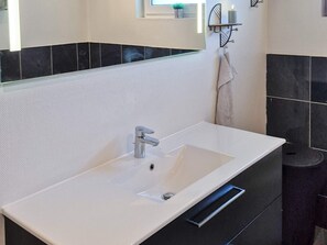 Ein modernes Badezimmer mit einem weißen Waschbecken, schwarzen Fliesen und einem Spiegel darüber.