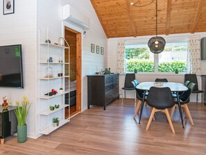 A dining area with a wooden ceiling, a round table with chairs, a TV on the wall, and a bookshelf with plants. - 8 Person Holiday Home in Hemmet-by Traum (Hemmet)