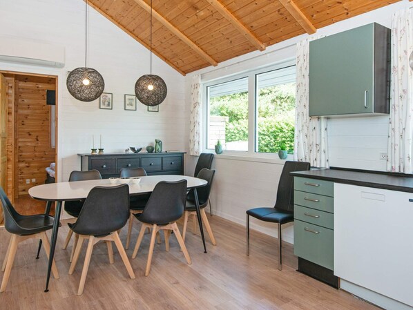A modern kitchen with a dining area, wooden ceiling, and large windows.