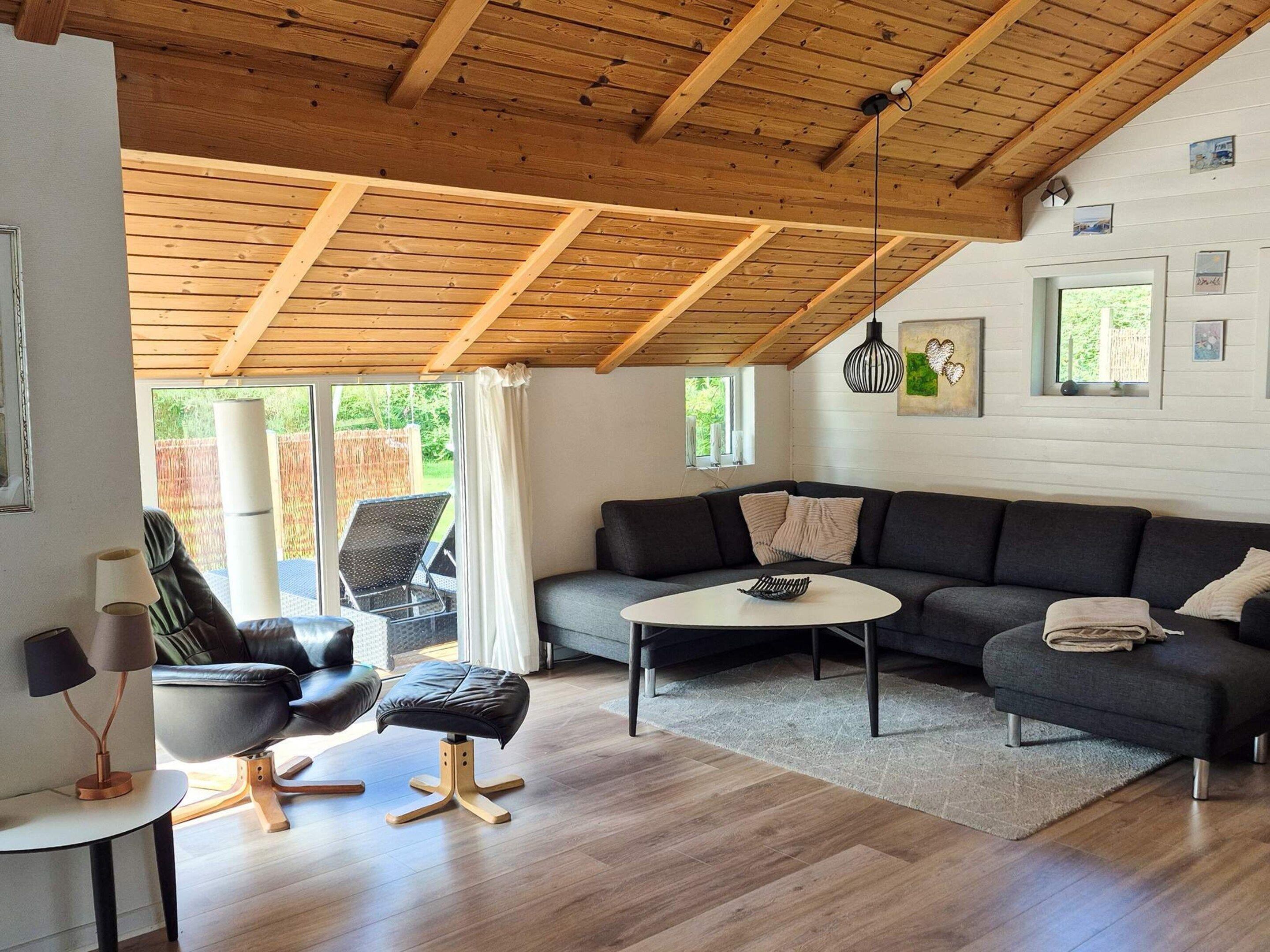 A modern living room with a wooden ceiling, a grey sofa, a black leather chair, and a small round table.