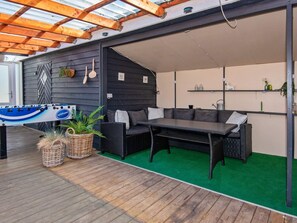 An outdoor seating area with a table and chairs, a pergola overhead, and a green artificial turf floor.