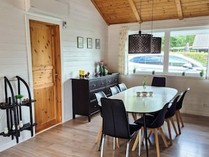 A dining area with a wooden ceiling, a white wall with horizontal lines, a black cabinet, a glass table, and black chairs.