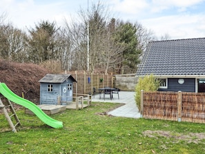 A backyard with a small playhouse, a slide, a table with chairs, and a fenced area.