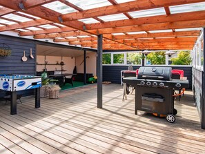 Une terrasse extérieure équipée d’un baby-foot, d’un barbecue et d’un espace salon abrité.