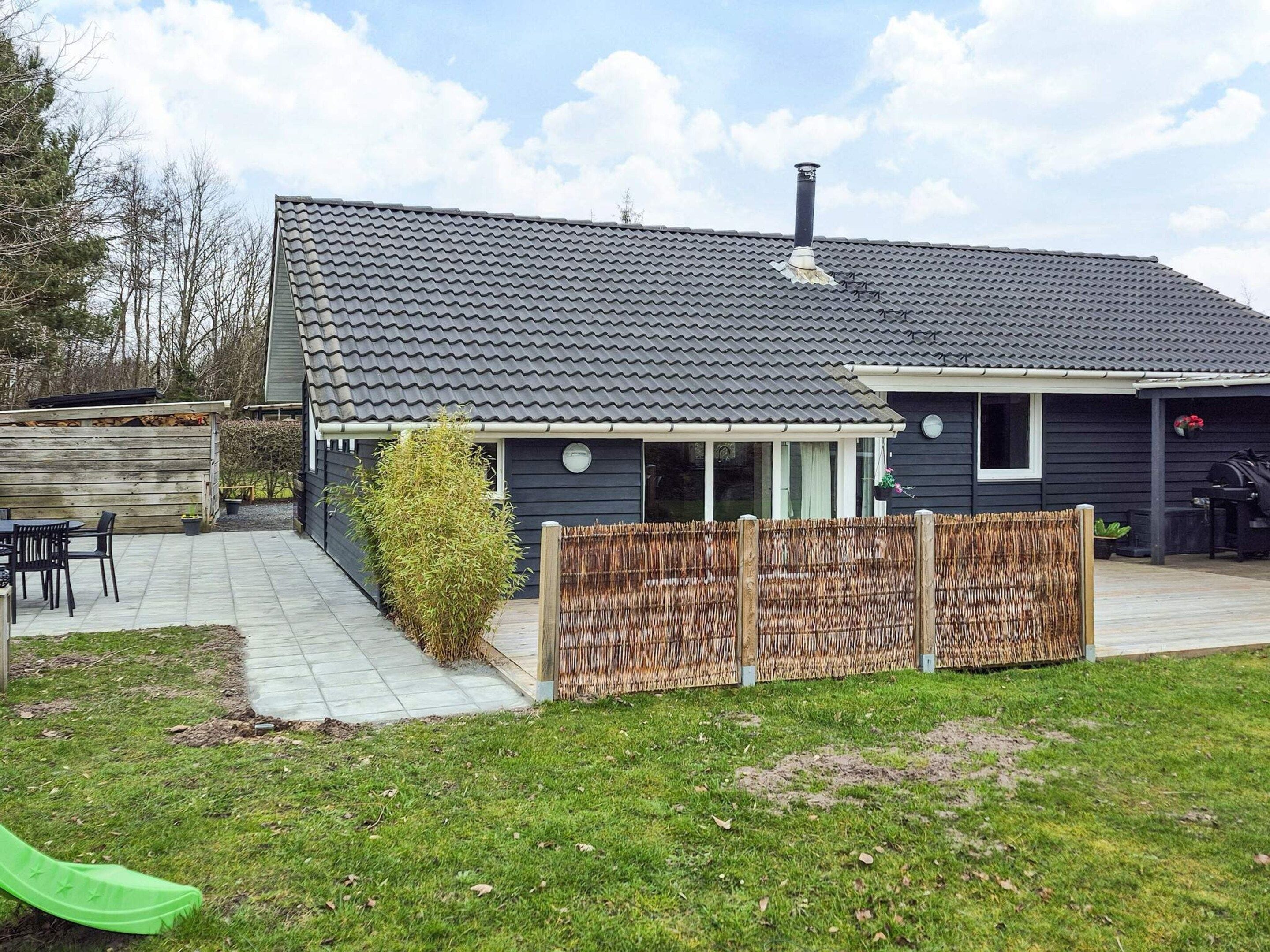 A house with a dark exterior, a tiled roof, a chimney, a covered patio, and a fenced yard.