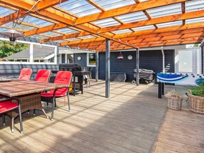 Um pátio externo com deck de madeira, uma mesa com cadeiras, churrasqueira e mesa de futebol de mesa.