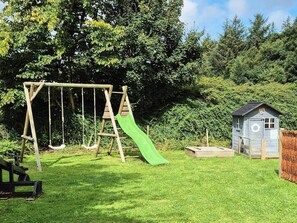 A wooden swing set with a green slide, a small shed, and a grassy yard.