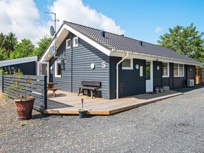 Ein zweistöckiges Gebäude mit dunkler Fassade, einer Holzterrasse und einer kleinen Sitzgelegenheit im Freien.