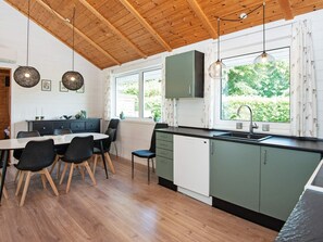 A modern kitchen with wooden ceiling beams, a dining area with a table and chairs, and a view of greenery outside.