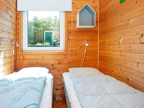 A wooden room with two beds, a window, and a hanging light fixture.