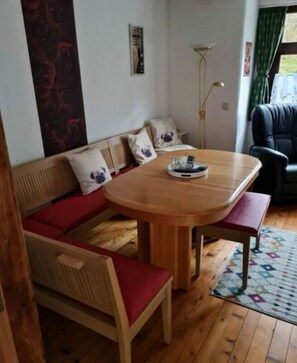 Una habitación acogedora con una mesa de madera, asientos con cojines rojos y una alfombra estampada.