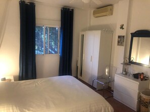 Une chambre avec un grand lit, une armoire, un miroir et une fenêtre avec des rideaux.
