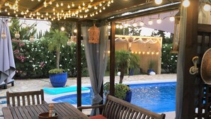 A wooden outdoor seating area with a pool in the background.