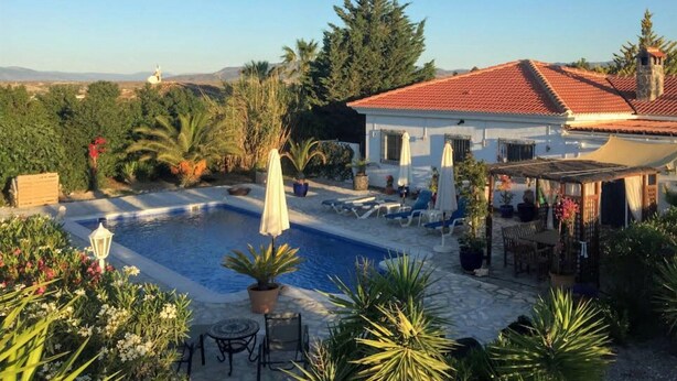 A poolside area with a white building, red-tiled roof, and outdoor seating.