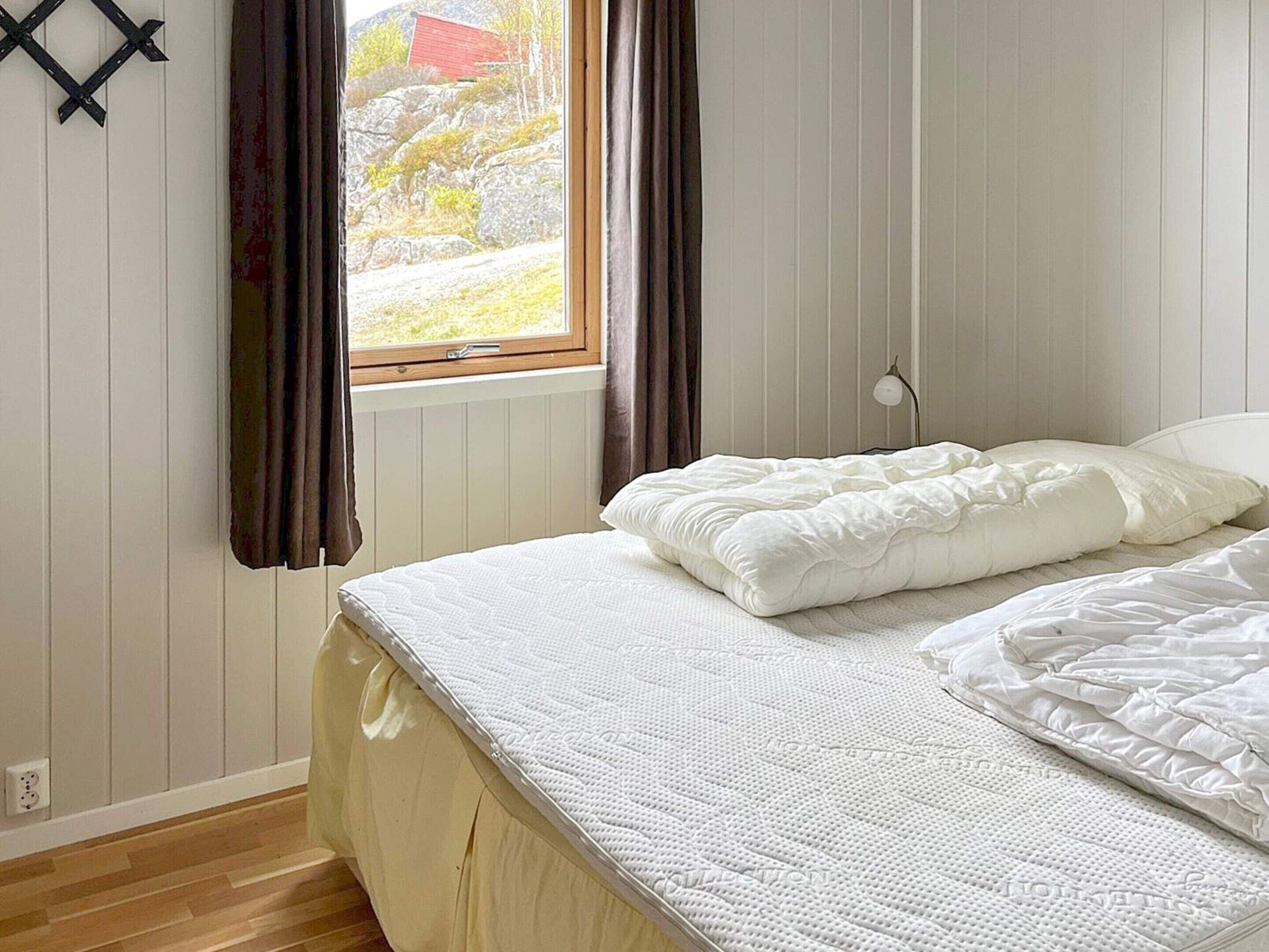A bedroom with a bed, a window with curtains, and a view of a red building outside.