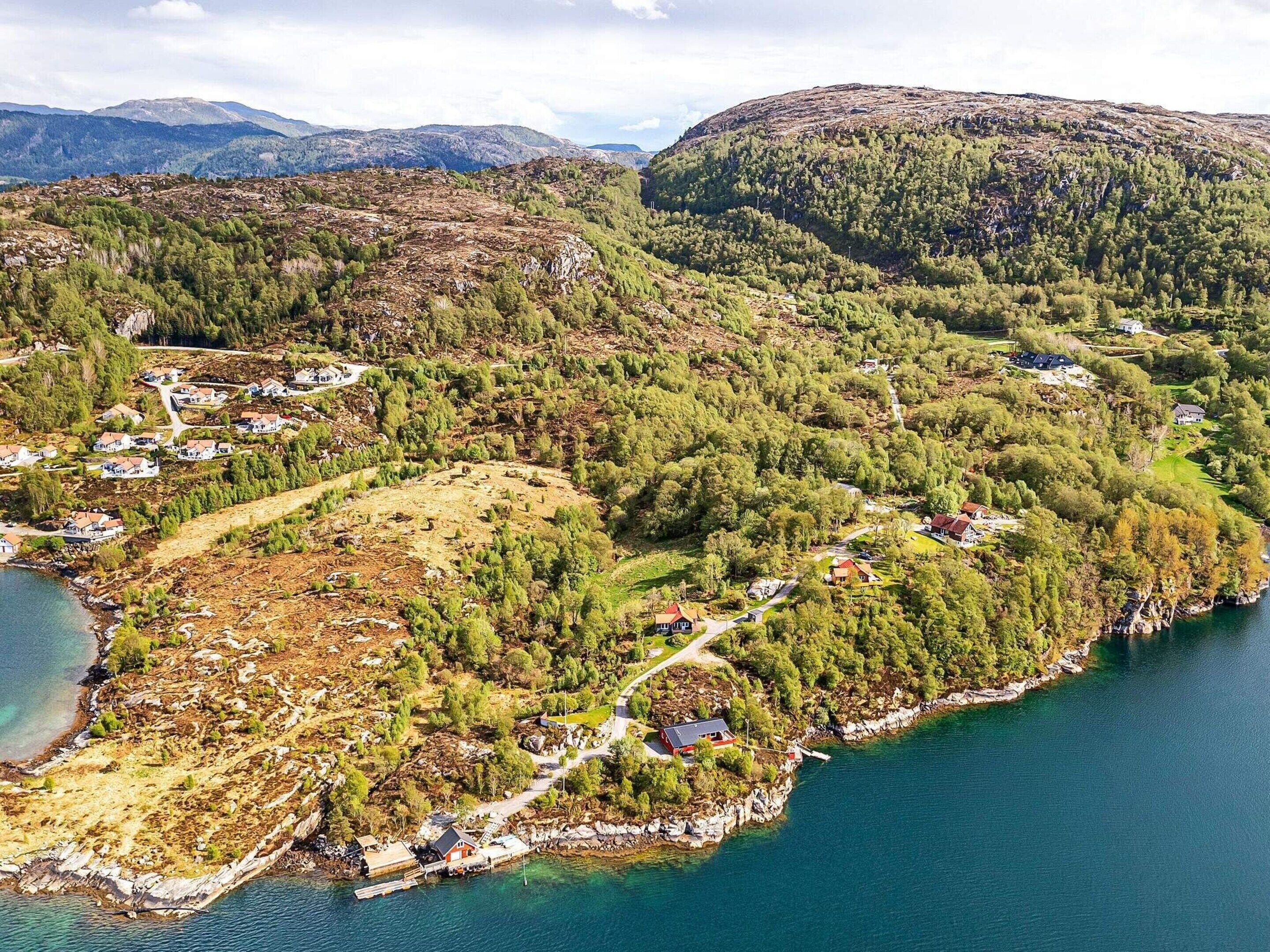 An aerial view of a coastal village with houses, a dock, and a clear view of the surrounding mountains and water.