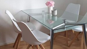 Uma sala de jantar moderna com mesa de vidro, cadeiras brancas e uma luminária pendente.