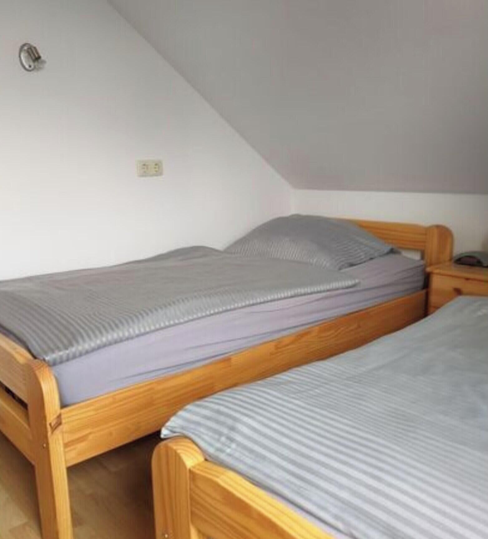Ein kleines, einzelnes Zimmer mit zwei Holzbetten, einem Nachttisch aus Holz und einer weißen Wand mit Steckdose.