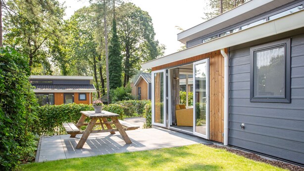A modern house with a patio, a wooden table, and a sliding glass door leading to an outdoor seating area. - Modern House With Roof in Rhenen (Rhenen)