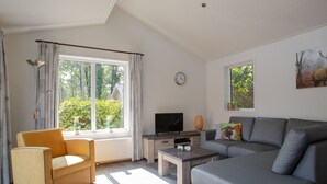 A modern living room with a sofa, armchair, TV, and a window with curtains. - Modern House With Roof in Rhenen (Rhenen)