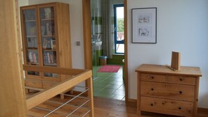 A room with a wooden bookshelf, a wooden dresser with drawers, a framed picture on the wall, and a door leading to another room. - Engemann Modern Retreat (Kassel)